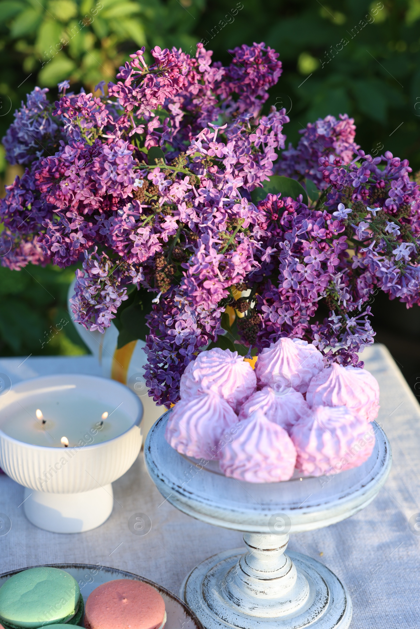 Beautiful lilac flowers, sweets and burning candles on table in garden, closeup Photo of Beautiful lilac flowers, sweets and burning candles on table in garden, closeup