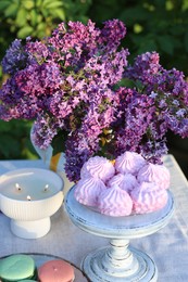 Photo of Beautiful lilac flowers, sweets and burning candles on table in garden, closeup