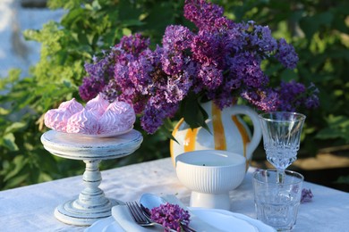 Photo of Beautiful lilac flowers, zephyrs, plates, cutlery, glasses and candle on table in garden