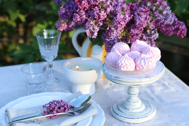 Photo of Beautiful lilac flowers, zephyrs, plates, cutlery, glasses and burning candle on table in garden