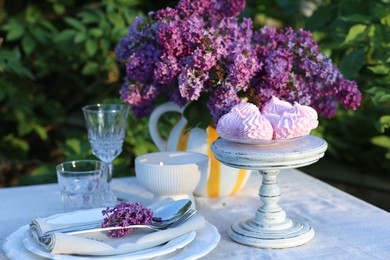 Photo of Beautiful lilac flowers, zephyrs, plates, cutlery, glasses and burning candle on table in garden