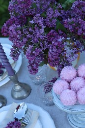 Photo of Beautiful lilac flowers, zephyrs, plates, cutlery and candles on table in garden, above view