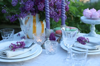 Photo of Beautiful lilac flowers, plates, cutlery, glasses and candles on table in garden, closeup