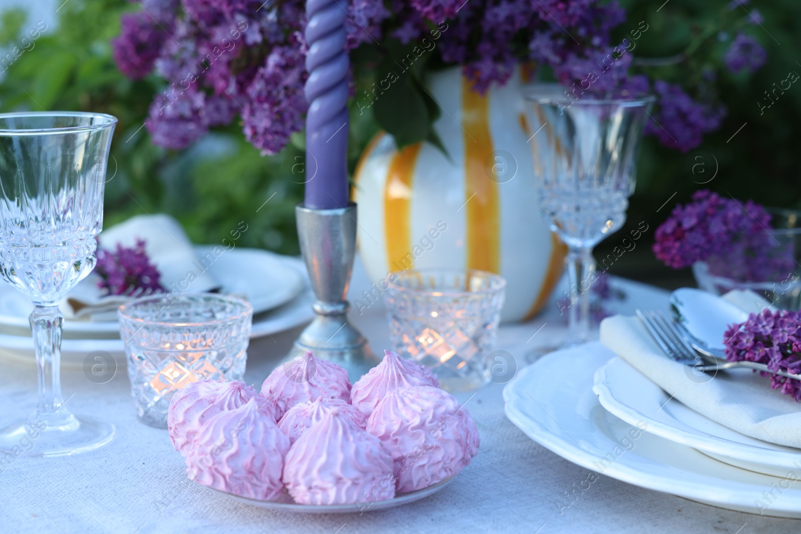 Photo of Beautiful lilac flowers, zephyrs, plates, cutlery, glasses and candles on table in garden, closeup