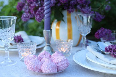 Photo of Beautiful lilac flowers, zephyrs, plates, cutlery, glasses and candles on table in garden, closeup