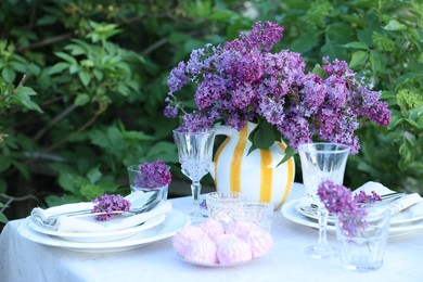 Photo of Beautiful lilac flowers, zephyrs, plates, cutlery and glasses on table in garden