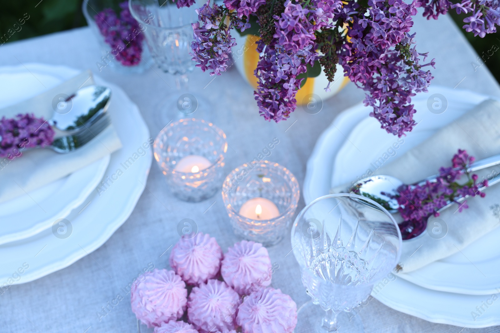 Beautiful lilac flowers, zephyrs, plates, cutlery, glasses and burning candles on table in garden, above view Photo of Beautiful lilac flowers, zephyrs, plates, cutlery, glasses and burning candles on table in garden, above view