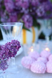 Photo of Beautiful lilac flowers, zephyrs and glass on table in garden, closeup. Space for text