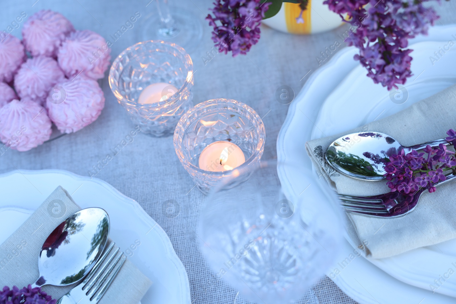 Beautiful lilac flowers, zephyrs, plates, cutlery, glasses and burning candles on table, above view Photo of Beautiful lilac flowers, zephyrs, plates, cutlery, glasses and burning candles on table, above view