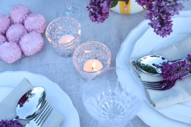 Photo of Beautiful lilac flowers, zephyrs, plates, cutlery, glasses and burning candles on table, above view