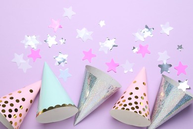 Photo of Beautiful party hats and confetti on lilac background, flat lay
