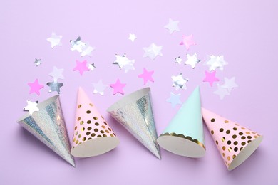 Photo of Beautiful party hats and confetti on lilac background, flat lay