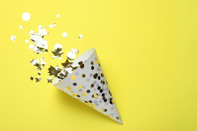 Photo of Beautiful party hat and confetti on yellow background, flat lay. Space for text