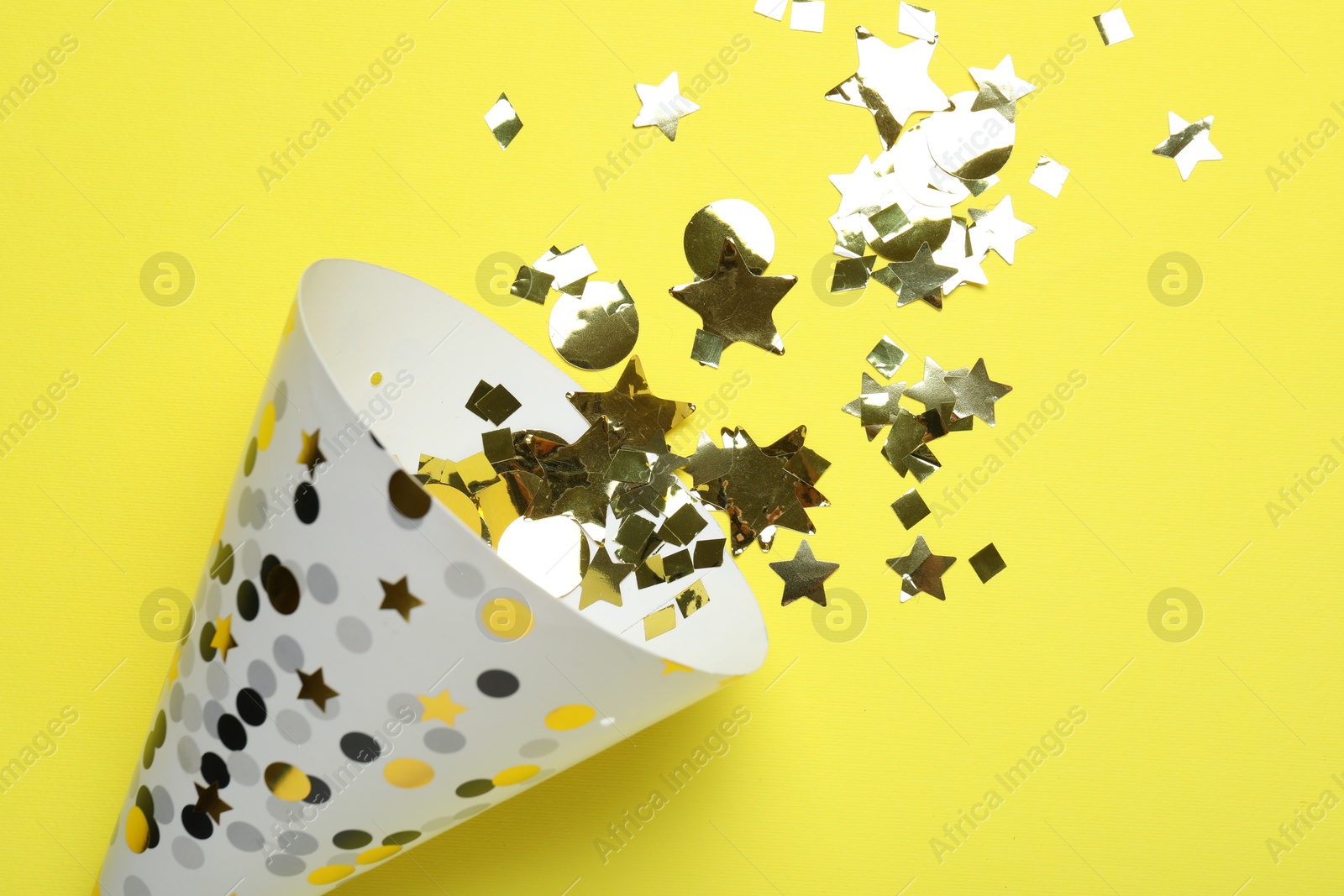 Beautiful party hat and confetti on yellow background, flat lay Photo of Beautiful party hat and confetti on yellow background, flat lay