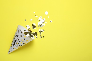 Photo of Beautiful party hat and confetti on yellow background, flat lay. Space for text
