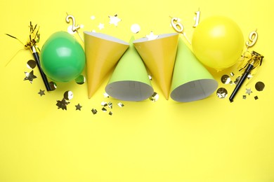 Photo of Beautiful party hats and other festive decor on yellow background, flat lay. Space for text