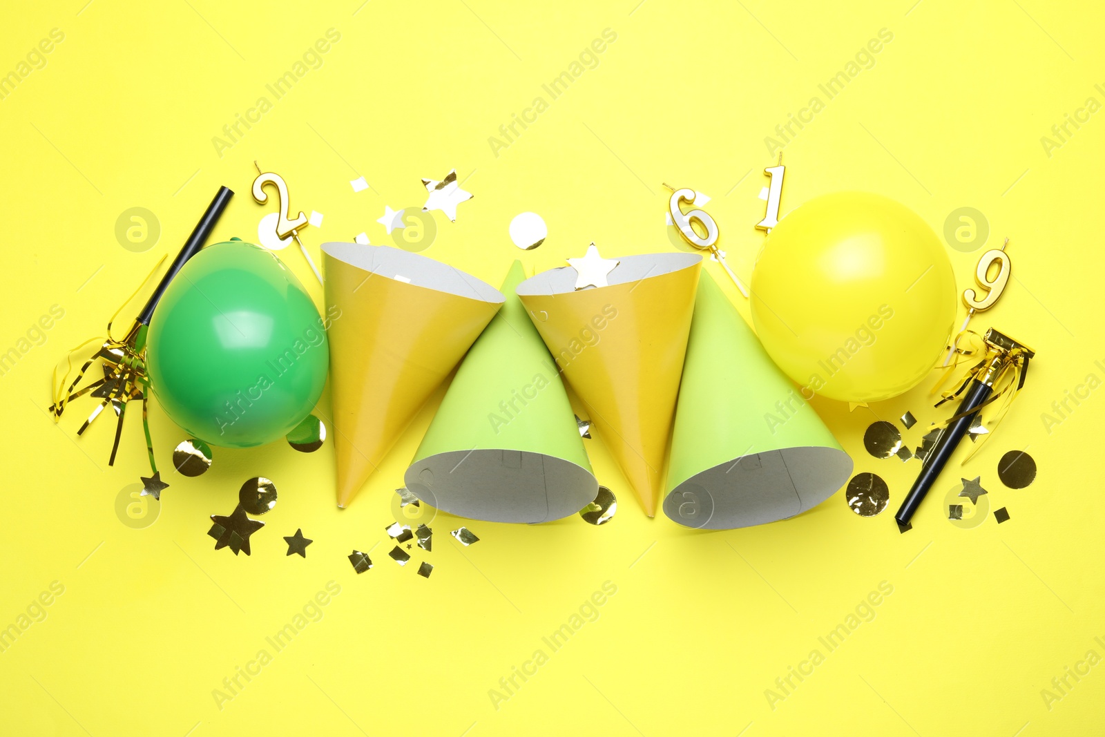 Beautiful party hats and other festive decor on yellow background, flat lay Photo of Beautiful party hats and other festive decor on yellow background, flat lay