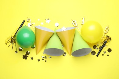 Photo of Beautiful party hats and other festive decor on yellow background, flat lay