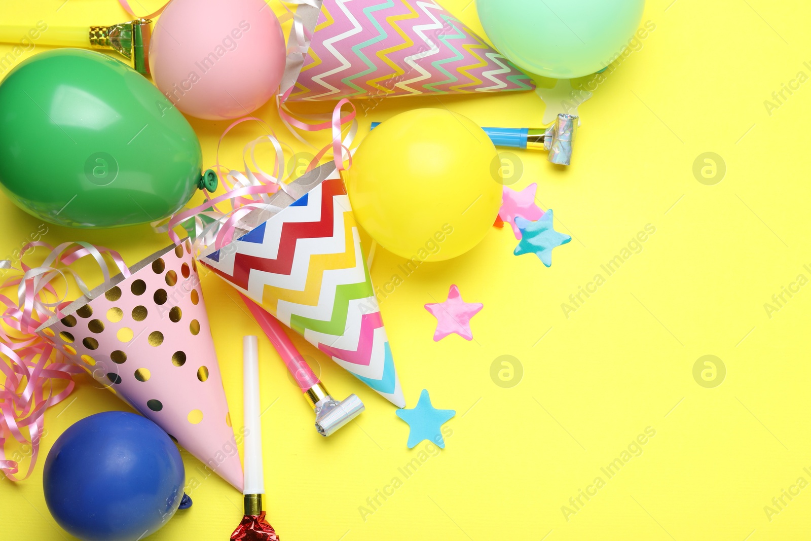 Beautiful party hats and other festive decor on yellow background, flat lay. Space for text Photo of Beautiful party hats and other festive decor on yellow background, flat lay. Space for text