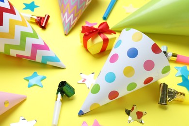 Photo of Beautiful party hats and other festive decor on yellow background, closeup
