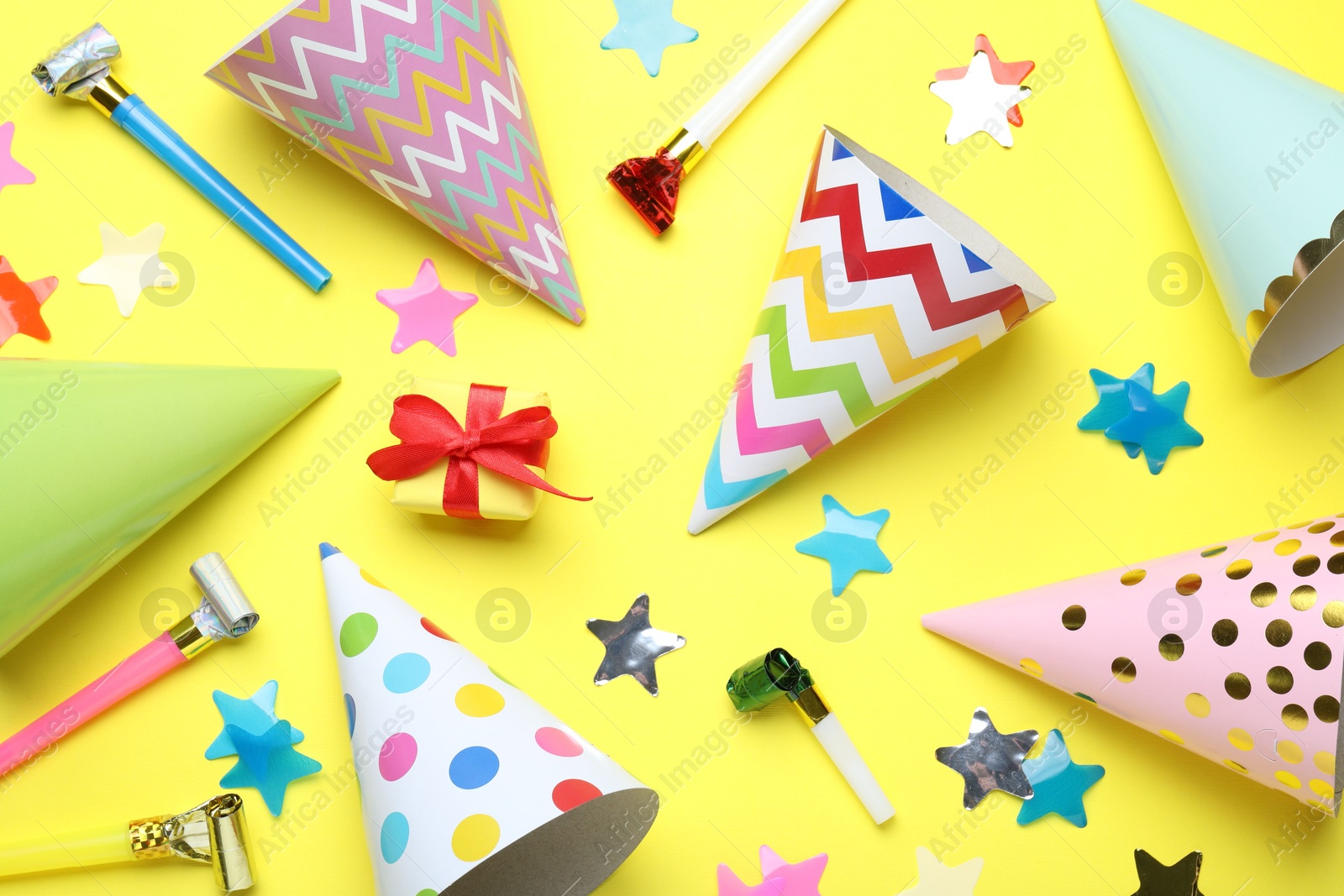 Beautiful party hats and other festive decor on yellow background, flat lay Photo of Beautiful party hats and other festive decor on yellow background, flat lay