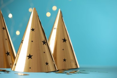 Photo of Beautiful party hats and confetti on light blue background, space for text. Bokeh effect