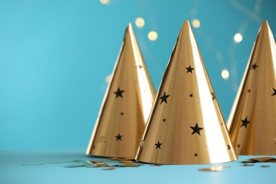 Photo of Beautiful party hats and confetti on light blue background, space for text. Bokeh effect