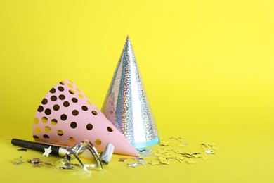Photo of Beautiful party hats and other festive decor on yellow background, space for text