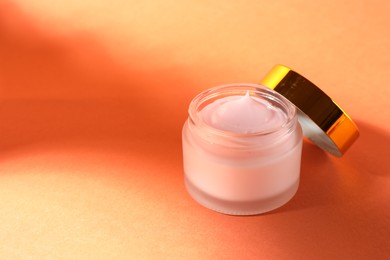 Photo of Jar of moisturizing body cream on orange background, closeup. Space for text