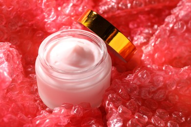Photo of Jar of moisturizing body cream on red bubble wrap, closeup