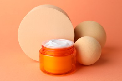 Photo of Stylish presentation of moisturizing body cream in jar on orange background, closeup