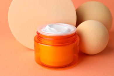Photo of Stylish presentation of moisturizing body cream in jar on orange background, closeup