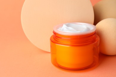 Photo of Stylish presentation of moisturizing body cream in jar on orange background, closeup. Space for text