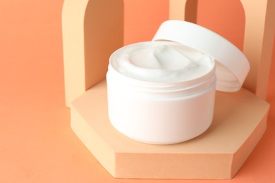 Photo of Stylish presentation of moisturizing body cream in jar on orange background, closeup. Space for text