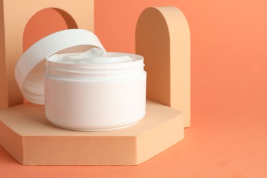 Photo of Stylish presentation of moisturizing body cream in jar on orange background, closeup. Space for text