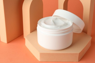 Photo of Stylish presentation of moisturizing body cream in jar on orange background, closeup