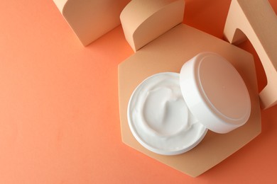 Photo of Stylish presentation of moisturizing body cream in jar on orange background, top view. Space for text