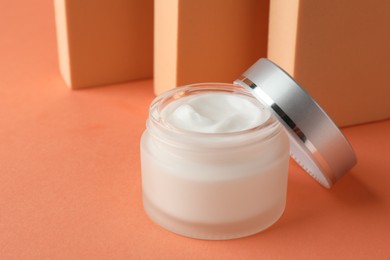 Photo of Stylish presentation of moisturizing body cream in jar on orange background, closeup. Space for text