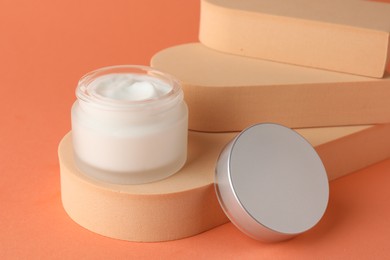 Photo of Stylish presentation of moisturizing body cream in jar on orange background, closeup