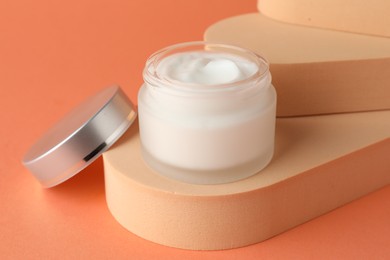 Photo of Stylish presentation of moisturizing body cream in jar on orange background, closeup