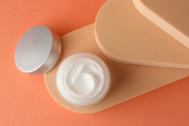Photo of Stylish presentation of moisturizing body cream in jar on orange background, top view