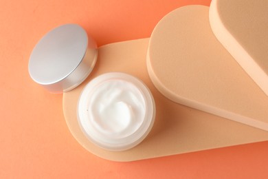 Photo of Stylish presentation of moisturizing body cream in jar on orange background, top view