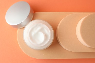 Photo of Stylish presentation of moisturizing body cream in jar on orange background, top view