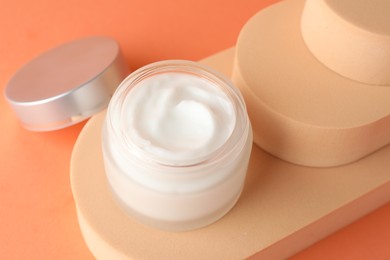 Photo of Stylish presentation of moisturizing body cream in jar on orange background, closeup