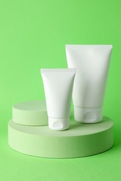 Photo of Stylish presentation of moisturizing body cream in tubes on light green background, closeup
