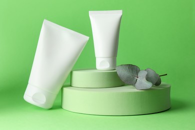 Photo of Stylish presentation of moisturizing body cream in tubes on light green background, closeup