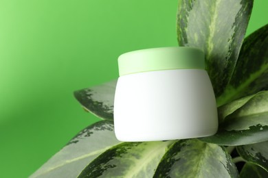 Photo of Jar of moisturizing body cream on plant against light green background, closeup. Space for text