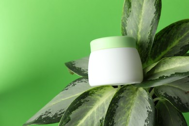 Photo of Jar of moisturizing body cream on plant against light green background, closeup. Space for text