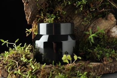 Photo of Jar of moisturizing body cream on tree bark with plants, closeup