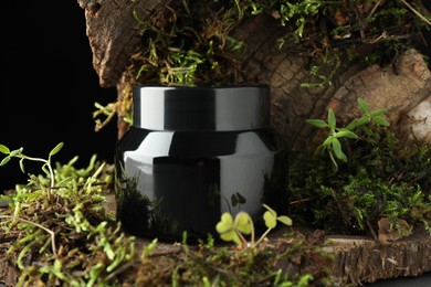 Photo of Jar of moisturizing body cream on tree bark with plants, closeup